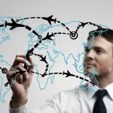 Mężczyzna rysuje na mapie świata trasy lotnicze, planując globalną logistykę.