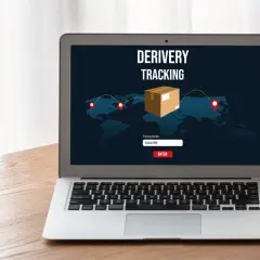 Laptop z ekranem pokazującym mapę świata i ikonę paczki. Widoczny jest napis "DERIVERY TRACKING" oraz pole do wpisania numeru przesyłki. To właśnie jest co to jest tracking.