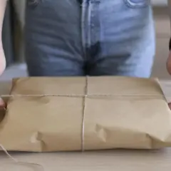 Ręce zawiązują sznurkiem paczkę owiniętą w brązowy papier. Prosty sposób, jak pakować paczki, by dotarły bezpiecznie.