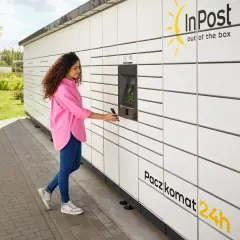 Kobieta z telefonem przy Paczkomacie InPost. Czy z paczkomatu można wysłać paczkę do domu? Tak, to wygodne rozwiązanie.