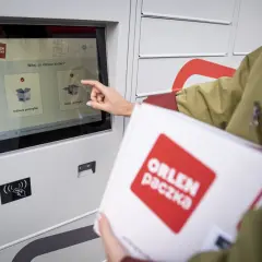 Kobieta z paczką ORLEN PACZKA dotyka ekranu automatu, wybierając opcję nadania przesyłki.