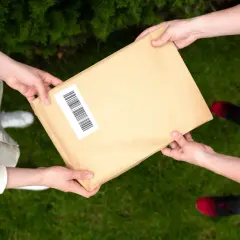 Dwie osoby przekazują sobie paczkę. Jedna z nich ma na rękawie białą koszulę, druga czerwoną bluzkę. Możliwe, że to anulowanie paczki InPost.