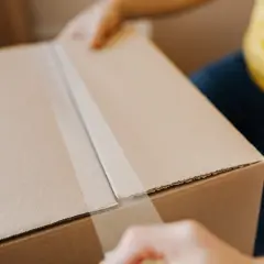 Osoba zamyka zapakowaną paczkę taśmą klejącą.