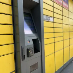Automat paczkowy InPost, do którego rozwozi kurier. Żółte skrzynki i szary panel sterowania.