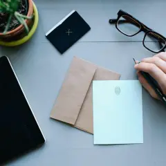 Ręka z ołówkiem przygotowuje się do napisania listu. Obok leżą koperta i papeteria, idealne, by dowiedzieć się, jak zaadresować list do Anglii.