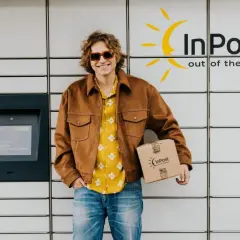 Uśmiechnięty mężczyzna z paczką InPost przy automacie. Sprawdza godziny graniczne InPost, by nadać przesyłkę.