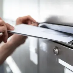 Ręce wkładają koperty do skrzynki pocztowej. To może być awizacja, co to jest, czyli powiadomienie o przesyłce.