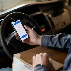 Kierowca w centrum logistycznym sprawdza trasę na telefonie, trzymając paczkę.