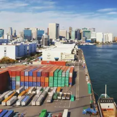 Kontenery czekają na załadunek. Ta wielka paczka do Japonii popłynie statkiem przez ocean, mijając nowoczesne miasto.