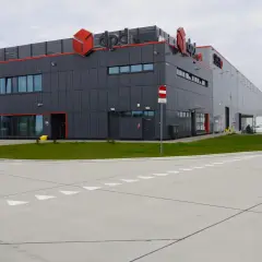 Nowoczesna sortownia DPD z charakterystycznym logo. Obok budynku parkują samochody dostawcze i osobowe.
