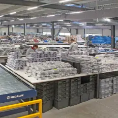 Pracownicy sortują odzież w magazynie. Widać taśmociąg, stoły z zapakowanymi produktami i pojemniki. To pokazuje różne funkcje magazynu.