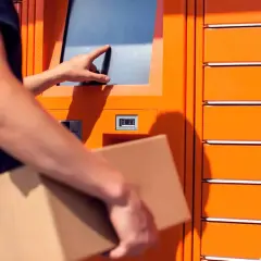 Odbiór paczki w automacie. Dłoń dotyka ekranu, a w drugiej ręce trzymana jest przesyłka. To wygodne rozwiązanie, jak paleta DHL.