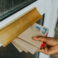 Dłoń wkłada listy do skrzynki. Na kopertach znaczki pocztowe, jakby z Kanady. Kod pocztowy jest kluczowy dla dostarczenia.