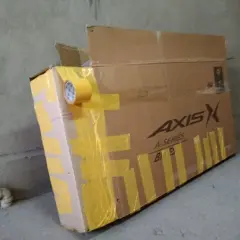 Duży karton na rower, zabezpieczony żółtą taśmą. Widoczne logo "AXIS A-SERIES".