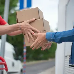 Kurier DPD przekazuje paczki klientce. Dwie osoby wymieniają się kartonami przed budynkiem.
