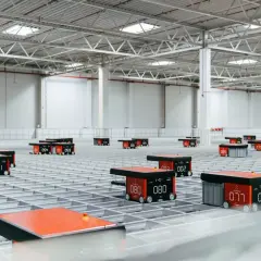 Nowoczesny magazyn z robotami realizującymi automatyzację logistyki. Mobilne jednostki poruszają się po siatce, usprawniając przepływ towarów.
