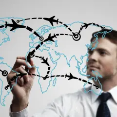 Mężczyzna rysuje na mapie świata trasy lotnicze, planując globalną logistykę.