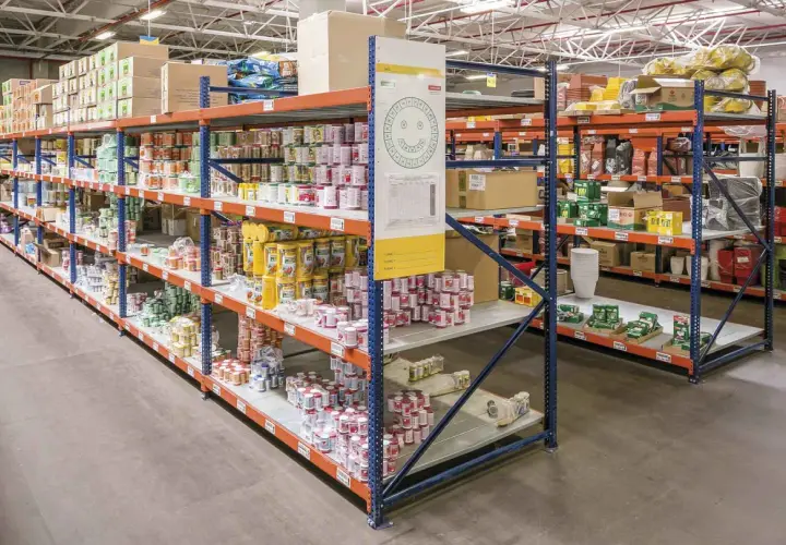 Wnętrze magazynu typu dark store z rzędami regałów wypełnionych produktami spożywczymi i innymi towarami.