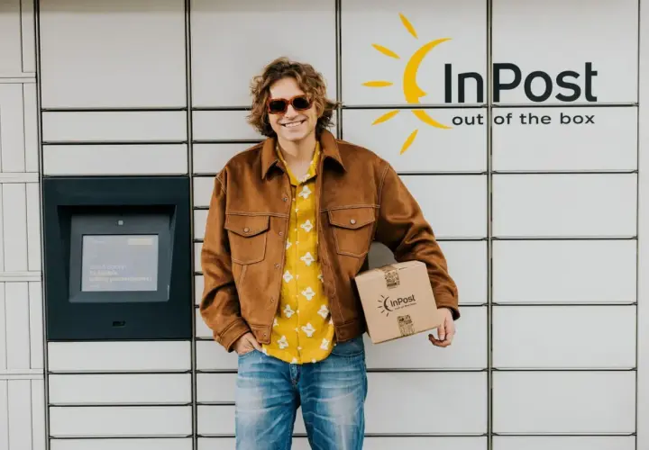 Uśmiechnięty mężczyzna z paczką InPost przy automacie. Sprawdza godziny graniczne InPost, by nadać przesyłkę.