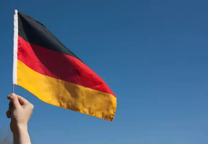 Dłoń trzyma flagę Niemiec na tle błękitnego nieba. Chcesz wiedzieć, jak zaadresować list do Niemiec?