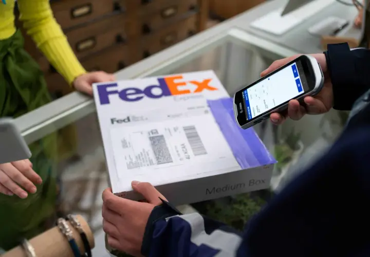 Osoba skanuje kod kreskowy na paczce FedEx za pomocą urządzenia mobilnego, realizując pointpack śledzenie.