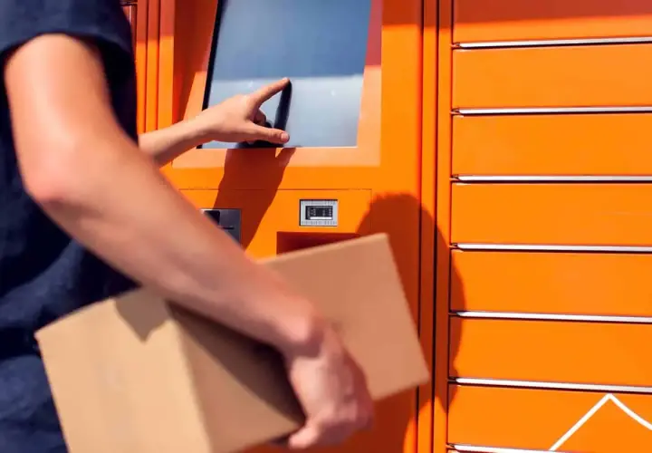Odbiór paczki w automacie. Dłoń dotyka ekranu, a w drugiej ręce trzymana jest przesyłka. To wygodne rozwiązanie, jak paleta DHL.