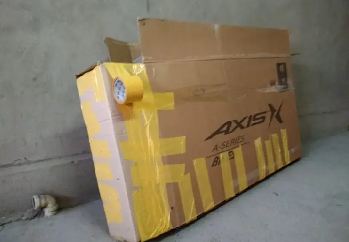 Duży karton na rower, zabezpieczony żółtą taśmą. Widoczne logo "AXIS A-SERIES".