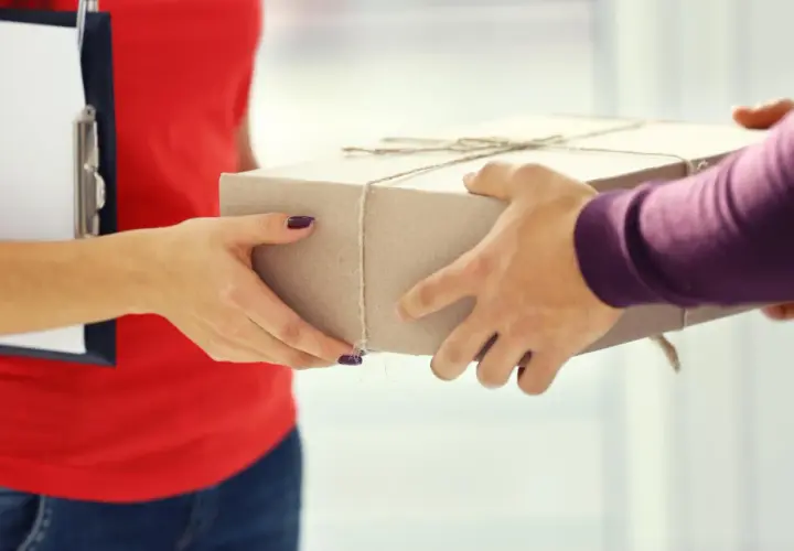 Przekazanie paczki w punkcie nadania DHL Express. Dwie pary rąk trzymają kartonowe pudełko.