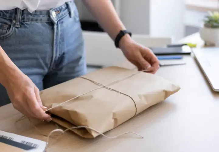 Ręce zawiązują sznurkiem paczkę w brązowym papierze. Gdzie nadać mini paczkę Poczta Polska?