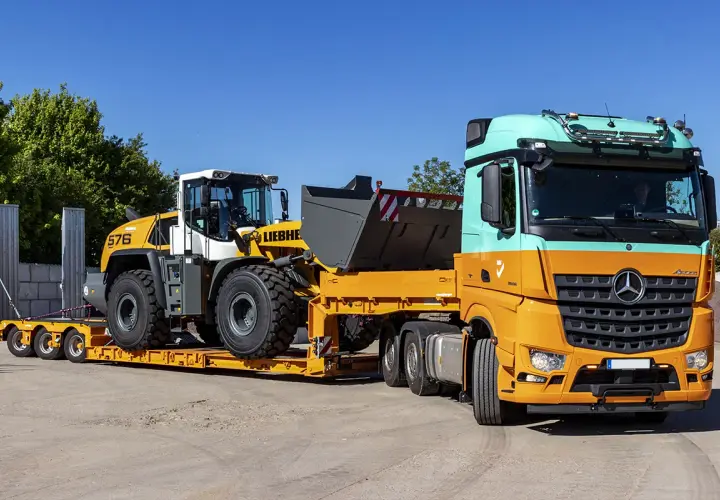 Pomarańczowo-miętowa ciężarówka transportuje ładowarkę kołową Liebherr na niskopodwoziowej przyczepie. Efektywny transport maszyn budowlanych.