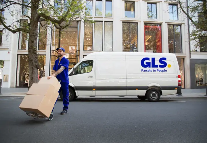 Kurier GLS z paczkami na wózku przed białym vanem. Dowiedz się, jak nadać paczkę z GLS.