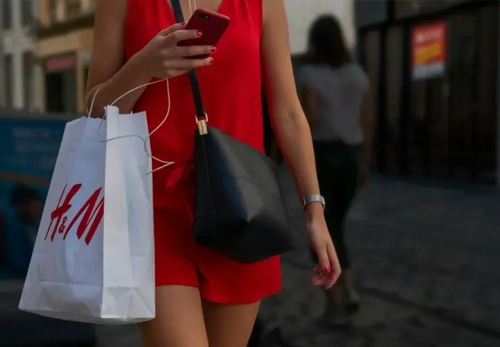 Kobieta w czerwonej sukience trzyma torbę z logo H&M. Zastanawia się, ile dni na zwrot ma zakupiony towar.