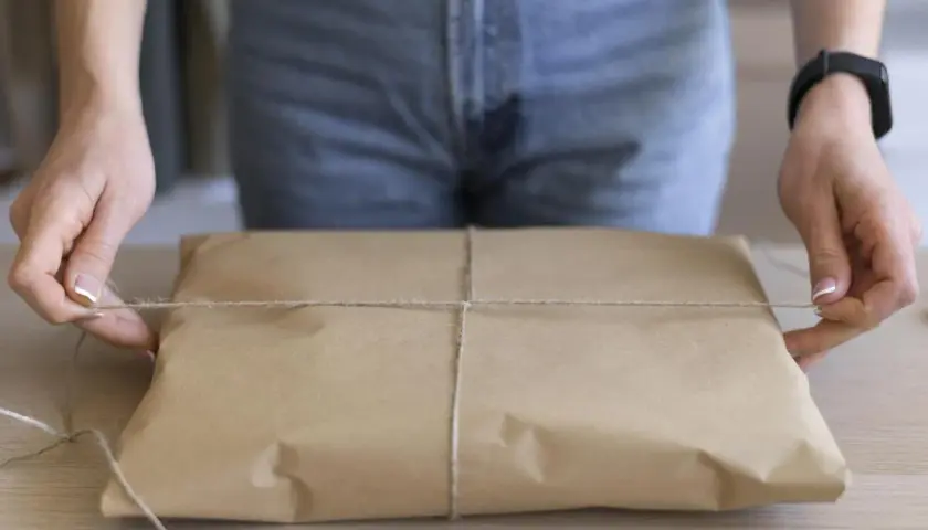 Ręce zawiązują sznurkiem paczkę owiniętą w brązowy papier. Prosty sposób, jak pakować paczki, by dotarły bezpiecznie.