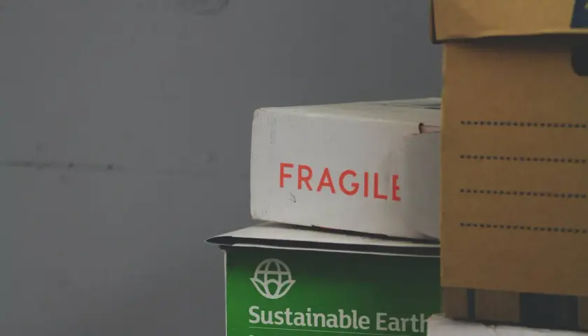 Paczka przyjęta w oddziale. Na białym kartonie napis "FRAGILE", pod nim zielony z napisem "Sustainable Earth". Obok brązowe pudło.