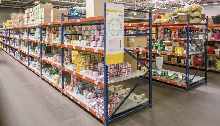 Wnętrze magazynu typu dark store z rzędami regałów wypełnionych produktami spożywczymi i innymi towarami.
