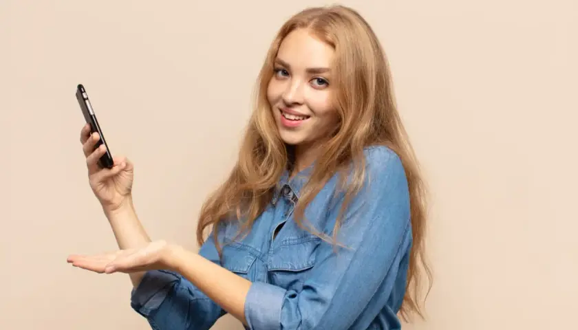 Uśmiechnięta blondynka trzyma telefon, prezentując etykietę cyfrową InPost.