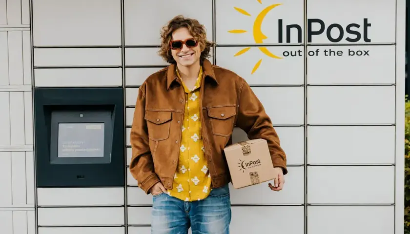 Uśmiechnięty mężczyzna z paczką InPost przy automacie. Sprawdza godziny graniczne InPost, by nadać przesyłkę.