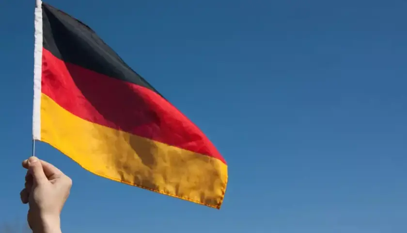Dłoń trzyma flagę Niemiec na tle błękitnego nieba. Chcesz wiedzieć, jak zaadresować list do Niemiec?