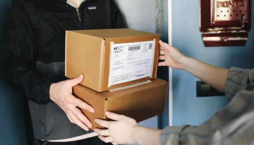 Dwie osoby przekazują sobie paczki. Na jednej z nich widoczna jest etykieta z kodem kreskowym. Ile cyfr ma kod nadania InPost?