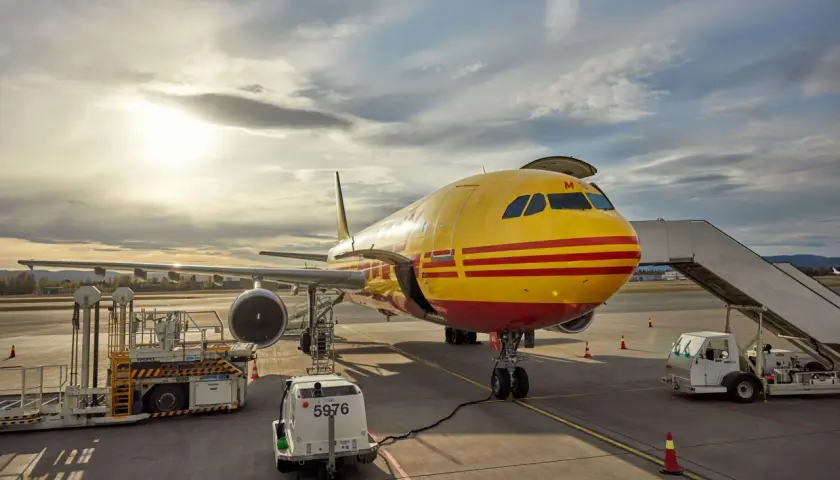 Żółty samolot DHL z czerwonymi pasami na płycie lotniska, gotowy do lotu do USA.