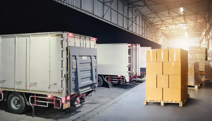 Ciężarówki czekają na załadunek w magazynie, gotowe do xpress delivery. Stosy paczek na paletach.