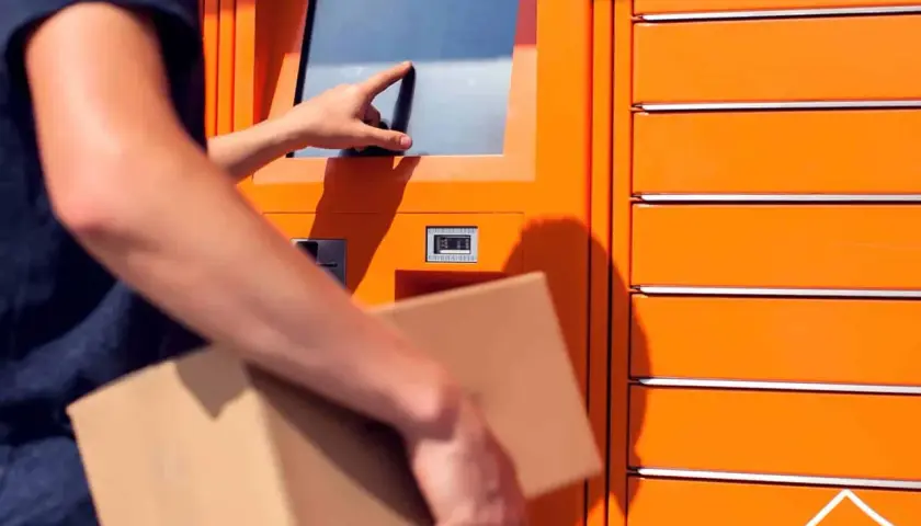Odbiór paczki w automacie. Dłoń dotyka ekranu, a w drugiej ręce trzymana jest przesyłka. To wygodne rozwiązanie, jak paleta DHL.