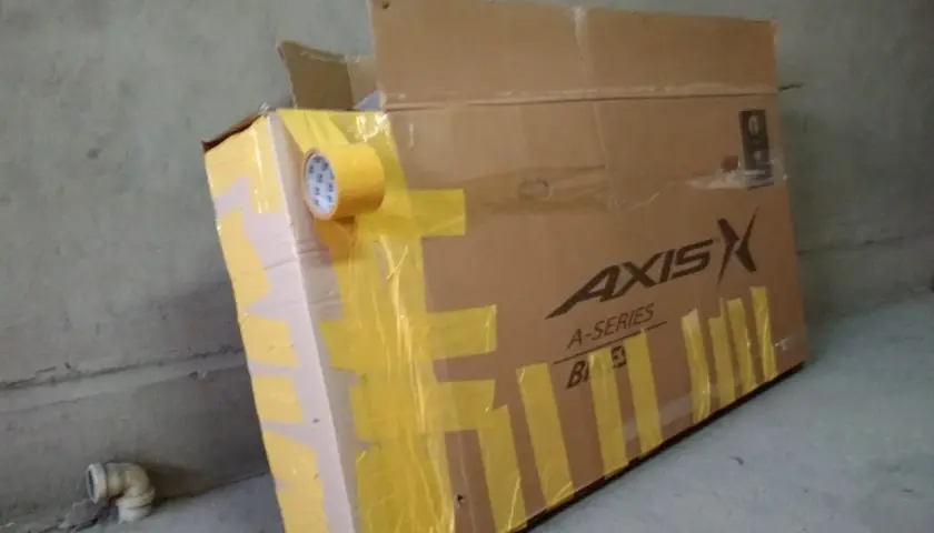 Duży karton na rower, zabezpieczony żółtą taśmą. Widoczne logo "AXIS A-SERIES".