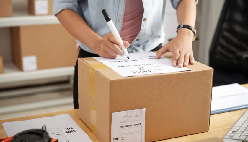 Osoba wypełnia etykietę na paczce, która może być zatrzymana przez urząd celny. Na etykiecie widnieje "FAST DELIVERY SERVICE".