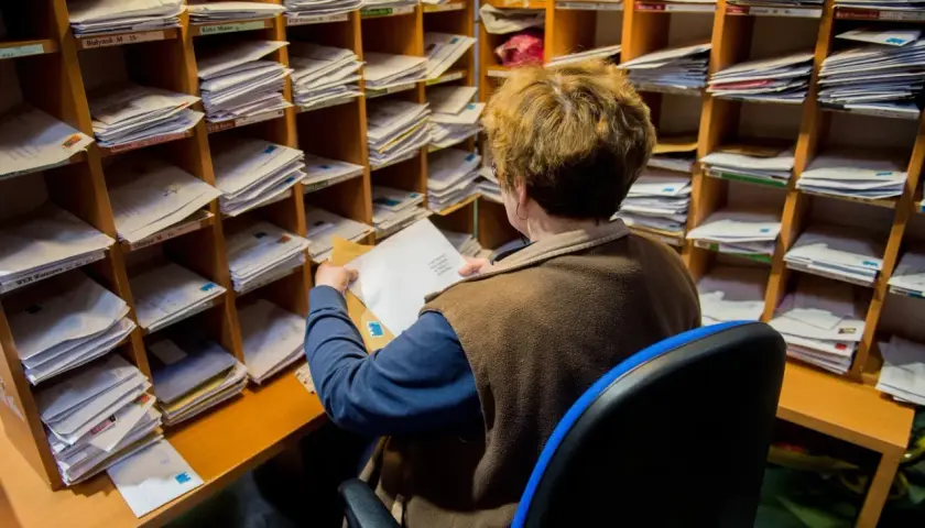 Pracownica sortuje listy w pocztowym regale. Zastanawia się, ile czasu na odebranie awizo, zanim zaginie w gąszczu przesyłek.