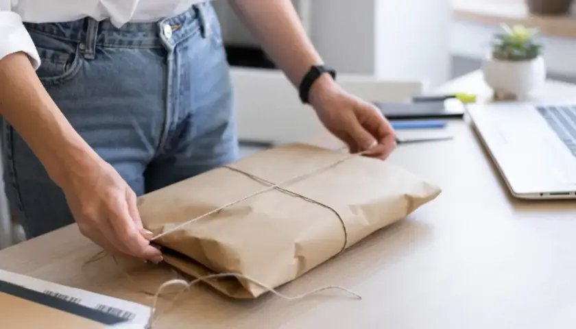 Ręce zawiązują sznurkiem paczkę w brązowym papierze. Gdzie nadać mini paczkę Poczta Polska?
