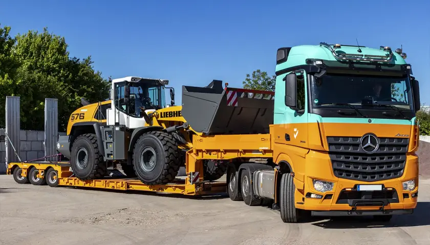 Pomarańczowo-miętowa ciężarówka transportuje ładowarkę kołową Liebherr na niskopodwoziowej przyczepie. Efektywny transport maszyn budowlanych.