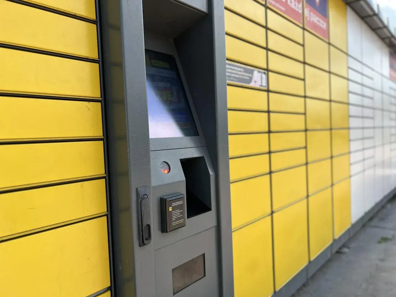Automat paczkowy InPost, do którego rozwozi kurier. Żółte skrzynki i szary panel sterowania.