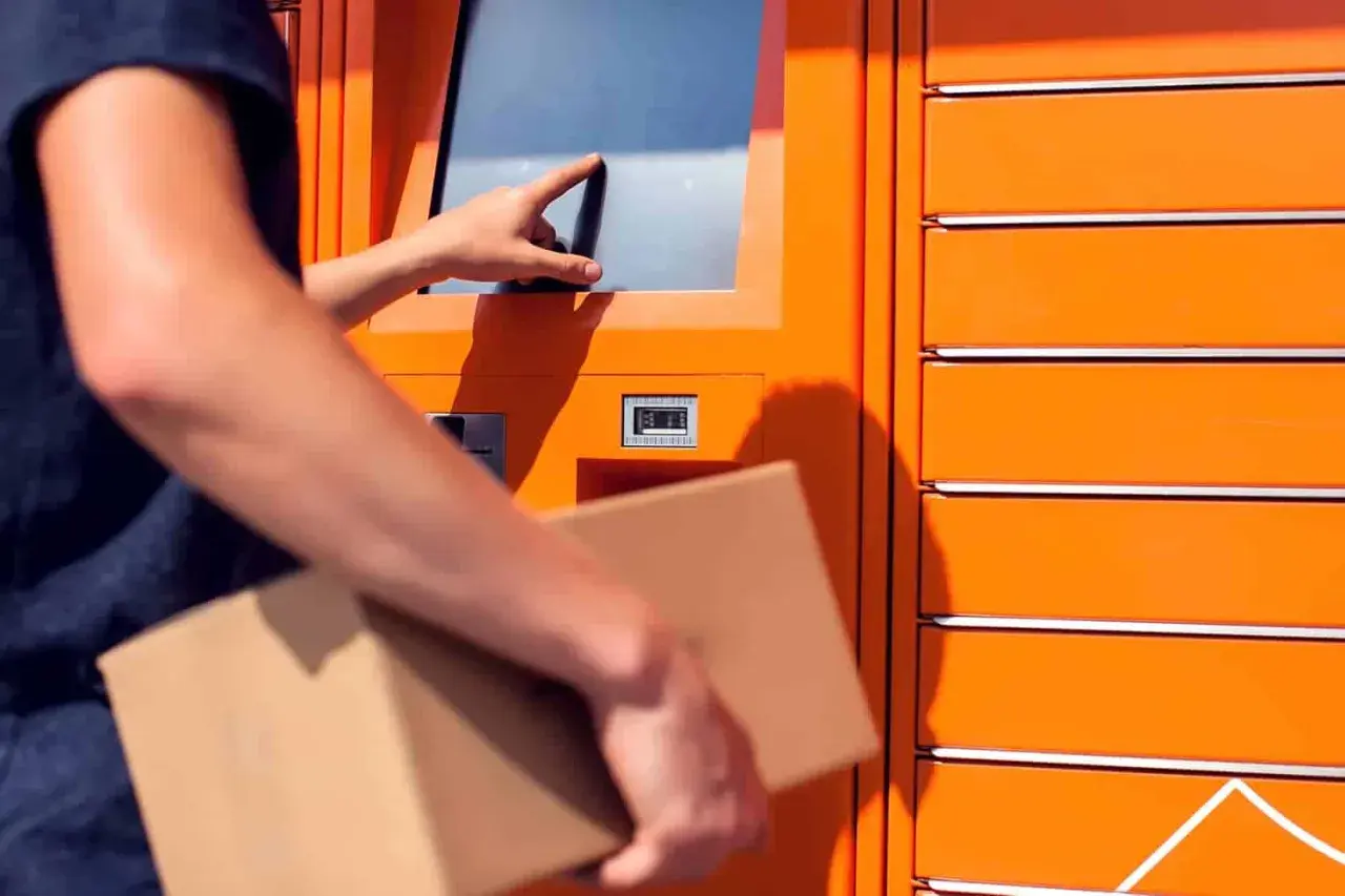 Odbiór paczki w automacie. Dłoń dotyka ekranu, a w drugiej ręce trzymana jest przesyłka. To wygodne rozwiązanie, jak paleta DHL.