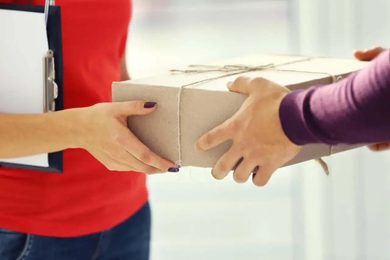 Przekazanie paczki w punkcie nadania DHL Express. Dwie pary rąk trzymają kartonowe pudełko.